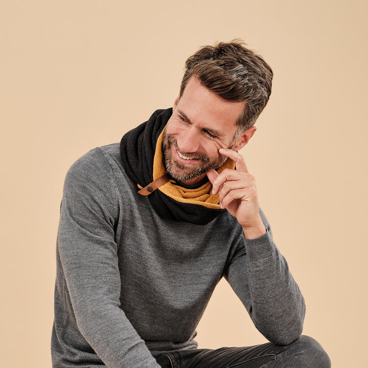 Gillio- warmer Loopschal, reversible in Senfgelb und Grau. man mit dem Schal an sitzt, schaut nach unten und lächelt. beige Hintergrund#farbe_anthrazit-mustard